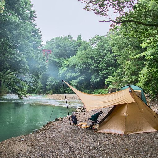 森の中の景色　左に川が流れており、左にキャンプテントが設置されている様子