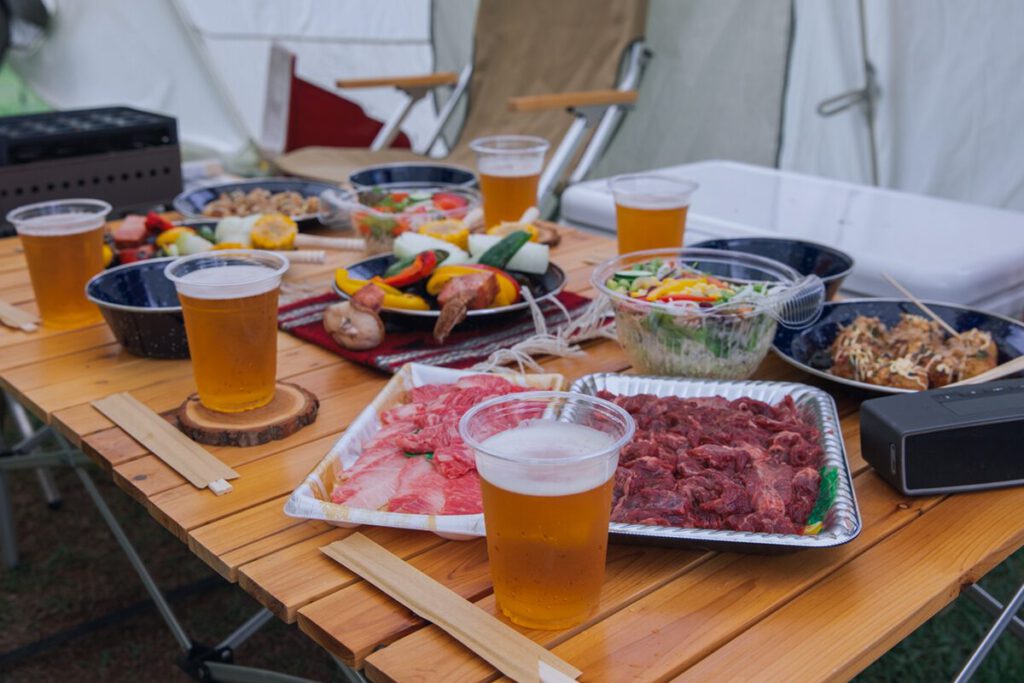机の上にバーベキュー用のお肉や野菜、サラダ、コップに注がれたビールなどが置かれている
