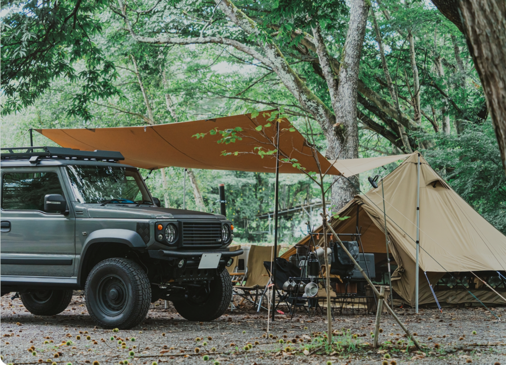 森の中で右側にキャンプテントが張られており、左側に車が駐車している様子
